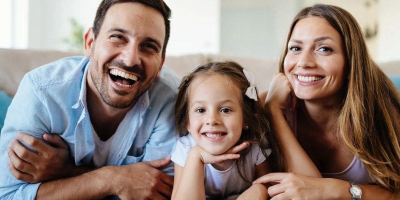 A family is smiling for the camera on the couch.