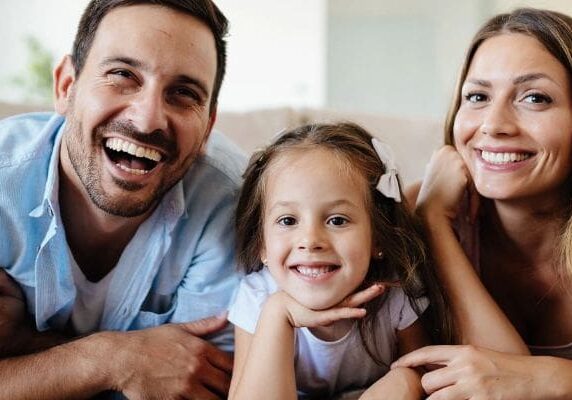 A family is smiling for the camera on the couch.